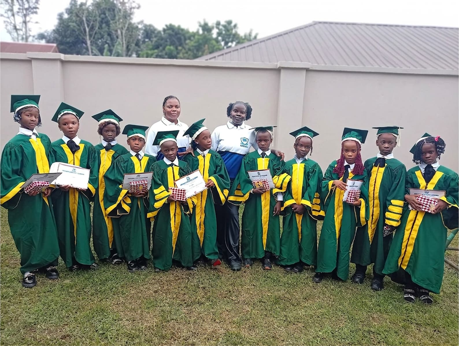 Magnam Grace pupils in green and gold graduation gowns with their teachers